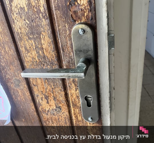 ידית דלת מתכת על דלת עץ ישנה ומתקלפת